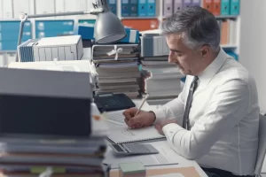 Businessman Working In The Office And Piles Of Paper