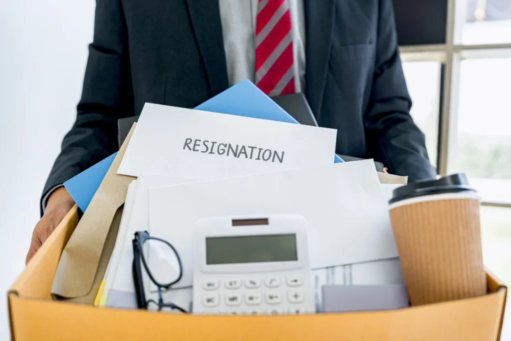 Employee Carrying All His Personal Belongings Into A Brown Cardboard Box With His Resignation Letter E1623215960322