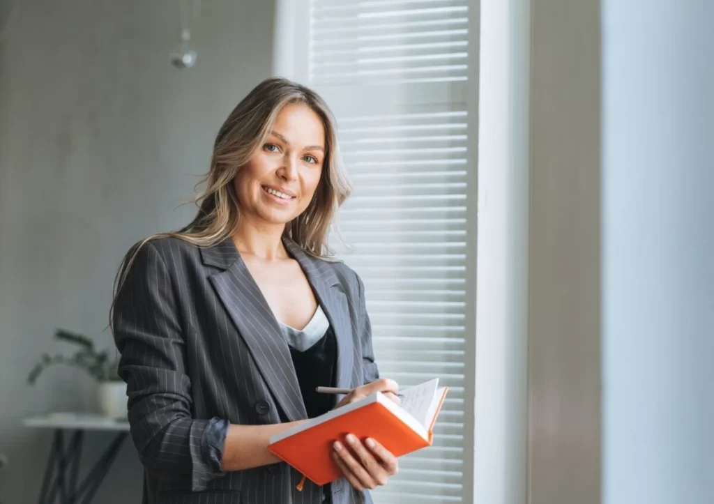 Professional Woman Holding Book Smiling E1658192013737