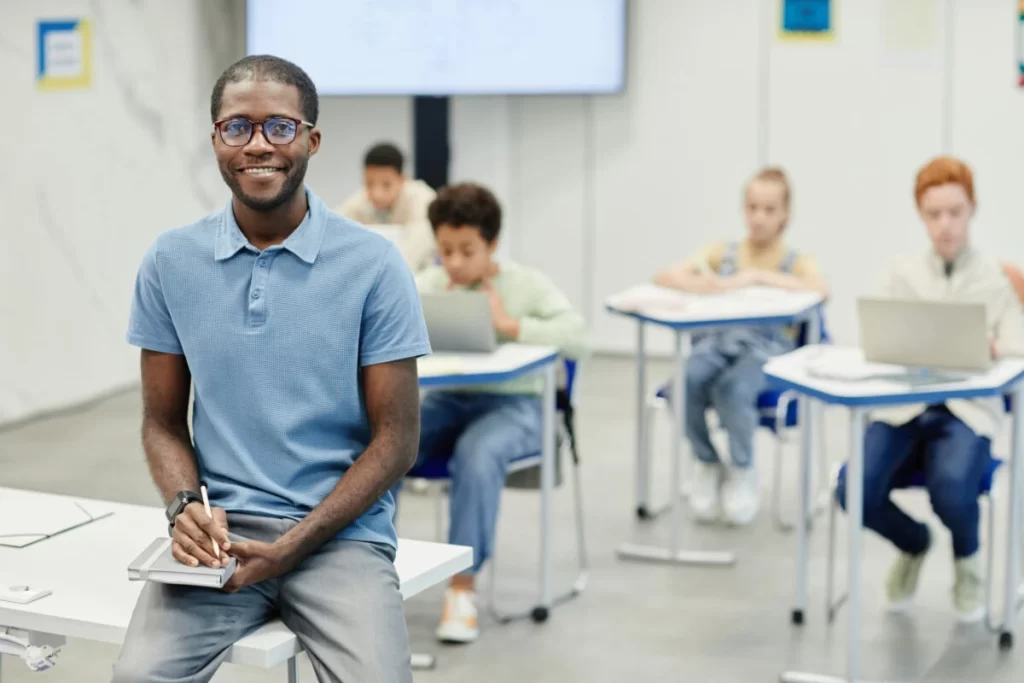 Smiling Teacher In School Classroom 2021 12 16 21 31 39 Utc Scaled E1665031425486