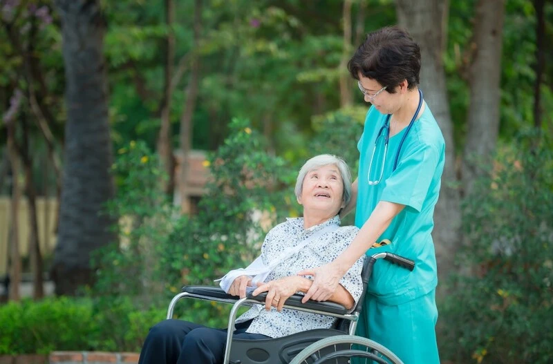 Cna Taking Care Of A Senior Patient Sitting On A Wheelchair