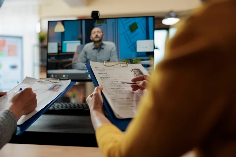 Hr Managers Watching A Video Resume While Holding Printed Resumes From Other Applicants