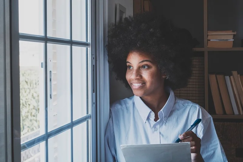 A Young Professional Contemplating And Writing Her 5 Year Goals On Paper