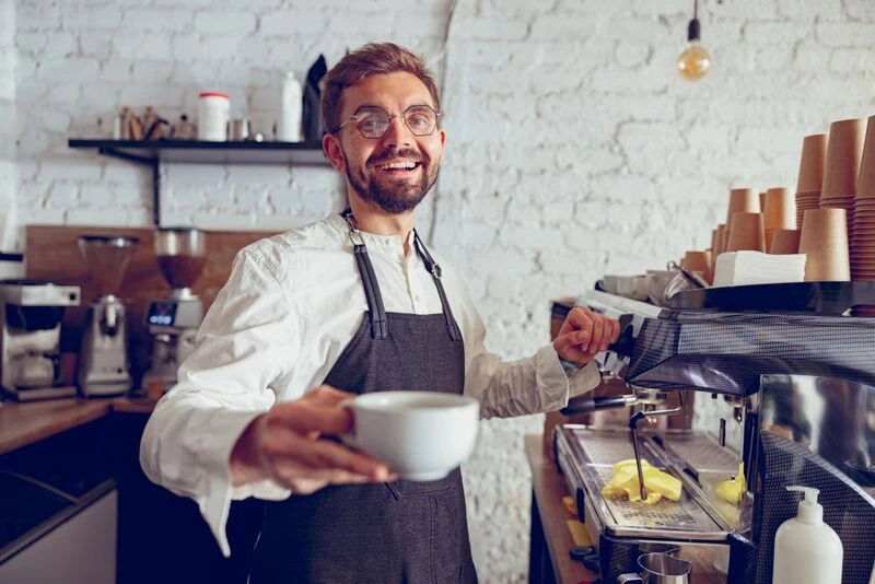 Male Barista Offering Coffee In Cafe