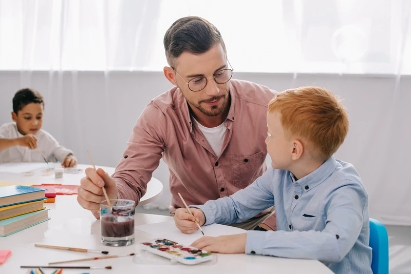 Teacher Helping A Little Boy Draw A Picture