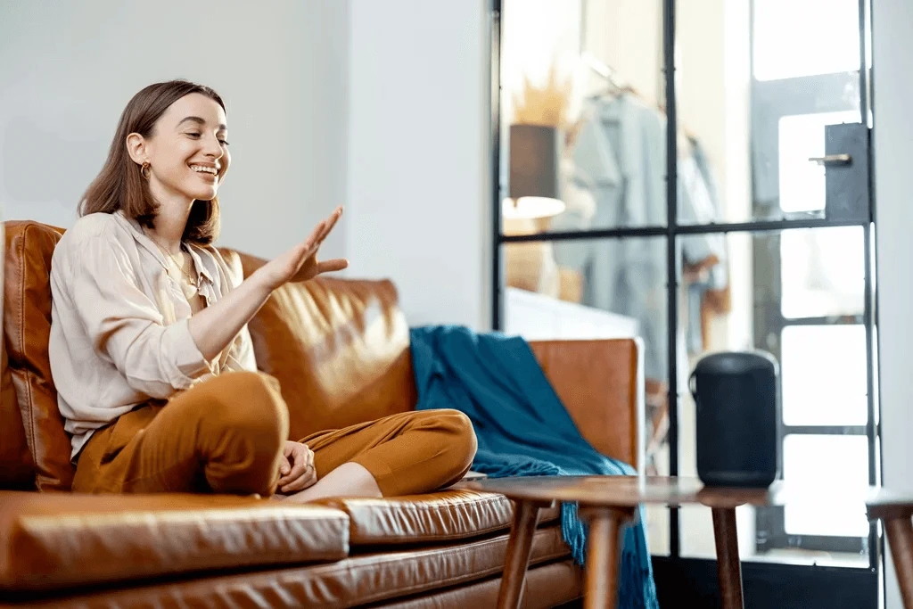 Woman Speaking With Audio Assistant Column On Sofa