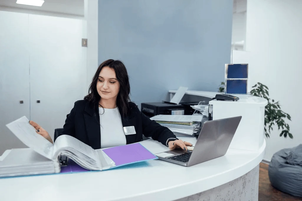 Receptionist Checking Login Details Of Visitors At The Desk