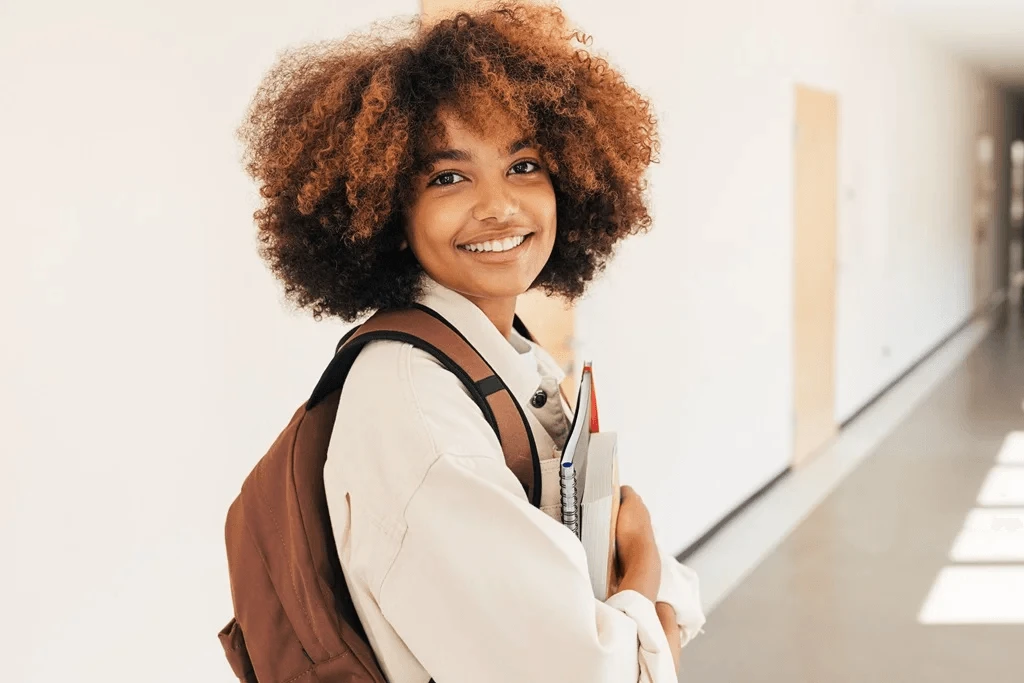 Smiling Student Standing In The Corridor While Holding Her Books