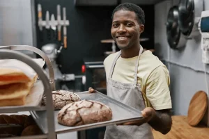 Baker Carefully Removing Freshly Baked Bread From The Oven