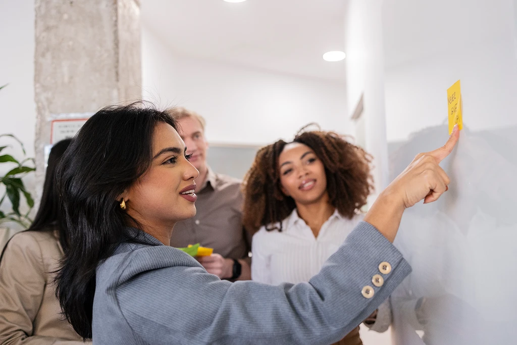 Businesswoman Pointing At Sticky Note During Brainstorming Session With Coworkers