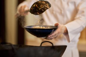 Skilled Chef Using Ladle For Taking Vegetables Out Of Wok