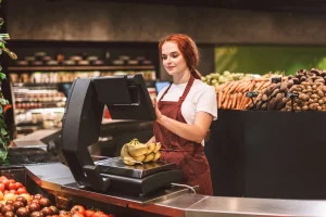 Young Smiling Seller In Apron Behind Counter