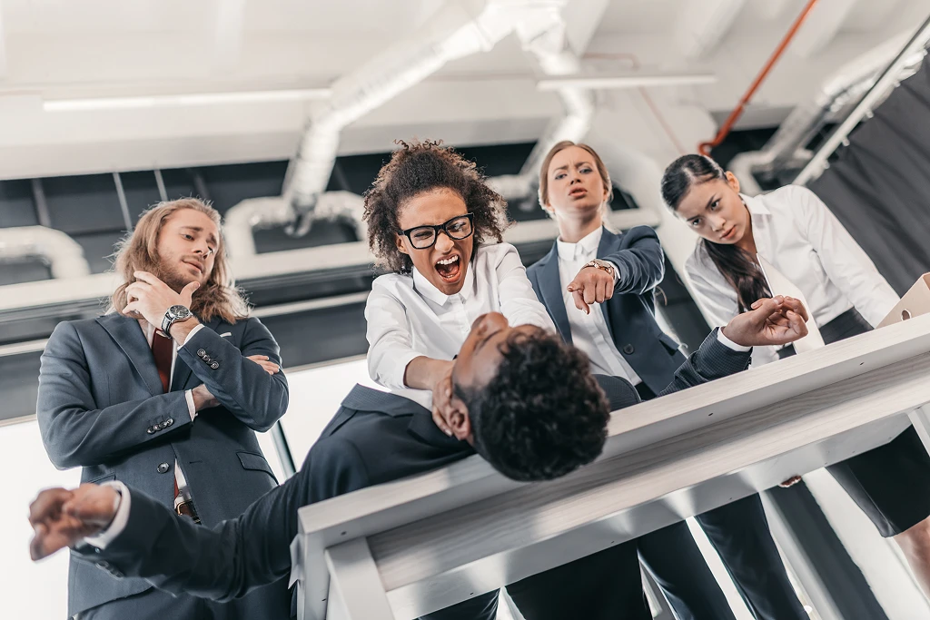 Three Young Angry Businesswomen Punishing Businessman Lying On Table